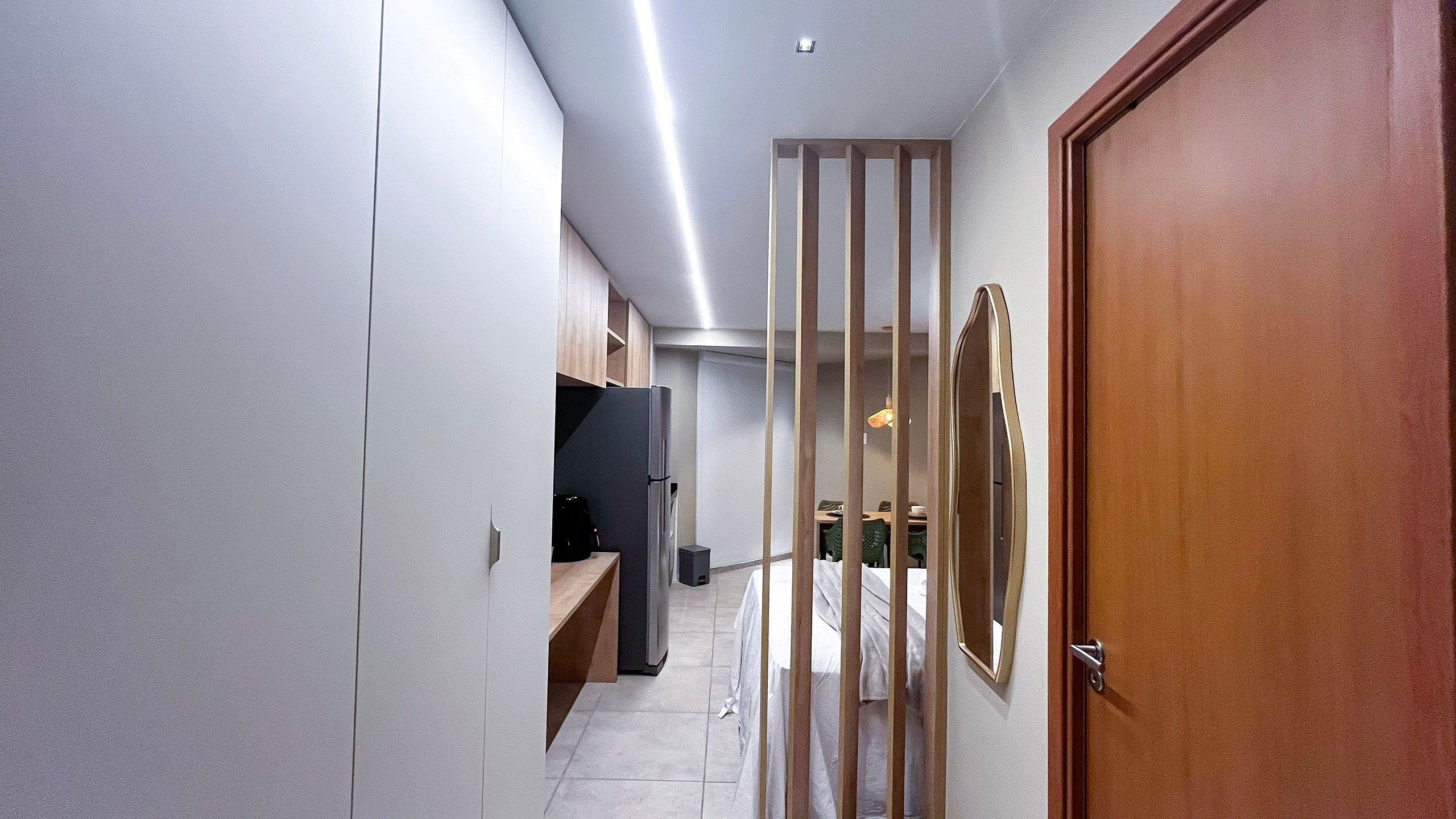 Un pasillo estrecho con una puerta de madera, un refrigerador y un televisor.