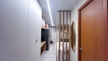 Un pasillo estrecho con una puerta de madera, un refrigerador y un televisor.
