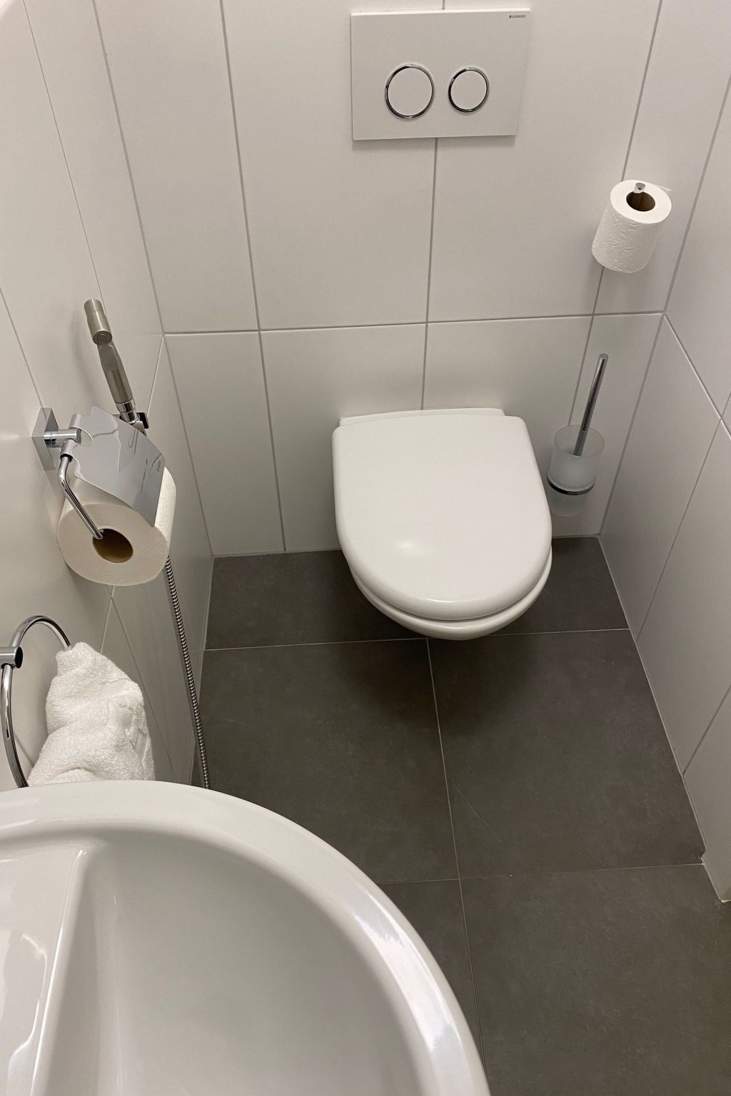 Ein Badezimmer mit Toilette, Bidet, Handtuchhalter und Toilettenpapierhalter.