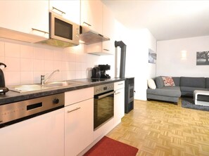 Eine moderne Küche mit Einbauofen, Mikrowelle und Kaffeemaschine, ein graues Sofa und ein roter Teppich.