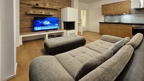 A modern living room with a flat-screen TV, a fireplace, a sofa, and a kitchen area. - 2_10 KitzNest Kaprun by Interhome (Kaprun)