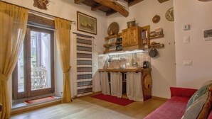 Ein gemütliches Zimmer mit Holzbalkendecke, einem roten Sofa, einer Küchenzeile mit Holzschränken und einem Esstisch mit Stühlen.