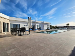 Un área de piscina moderna al aire libre con comedor y sillas de descanso.