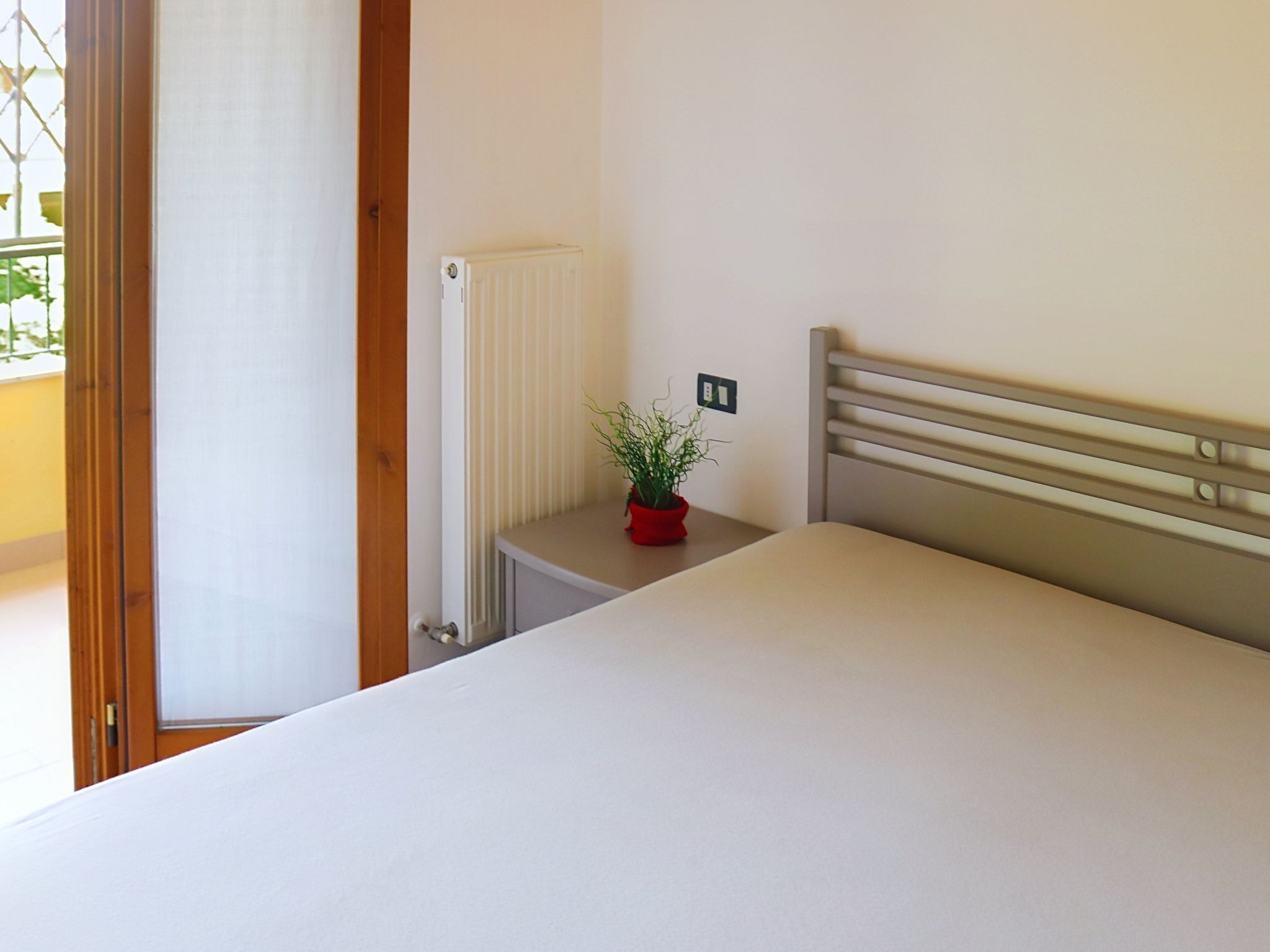 Une chambre à coucher avec un lit, un radiateur, une plante en pot et une fenêtre.