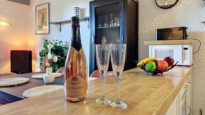 Une bouteille de champagne Glod-Mauchamp, deux verres, un panier de fruits, un four à micro-ondes et un meuble dans une pièce dont le mur est texturé et orné d’un tableau encadré.