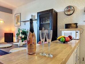 Eine Flasche Glod-Mauchamp Champagner, zwei Gläser, eine Obstschale, eine Mikrowelle und ein Schrank in einem Raum mit strukturierter Wand und einem gerahmten Bild.