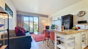 Un salon moderne avec un canapé, un coin repas comprenant une table et des chaises, une cuisine équipée d’un four à micro-ondes, et une vue sur l’extérieur grâce à une porte coulissante.