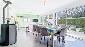 Eine moderne Küche mit Einbauherd, ein Essbereich mit großem Tisch und Stühlen sowie ein Blick ins Freie durch große Fenster.