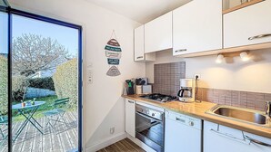 Una cucina moderna con mobili bianchi, piano cottura a gas, forno e lavastoviglie. Una finestra offre vista su un giardino.