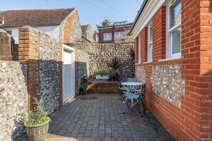 Ein schmaler Innenhof mit Steinmauer, kleinem Garten und Tisch mit Stühlen.