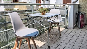 Un balcón con una mesa y sillas, una planta en maceta y una barandilla de metal.