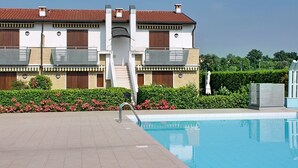 Un edificio moderno con piscina, escalera cubierta y jardín con flores rosadas.