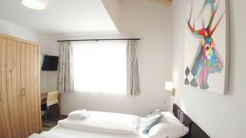 A bedroom with a bed, a wooden wardrobe, a television, and a painting on the wall.