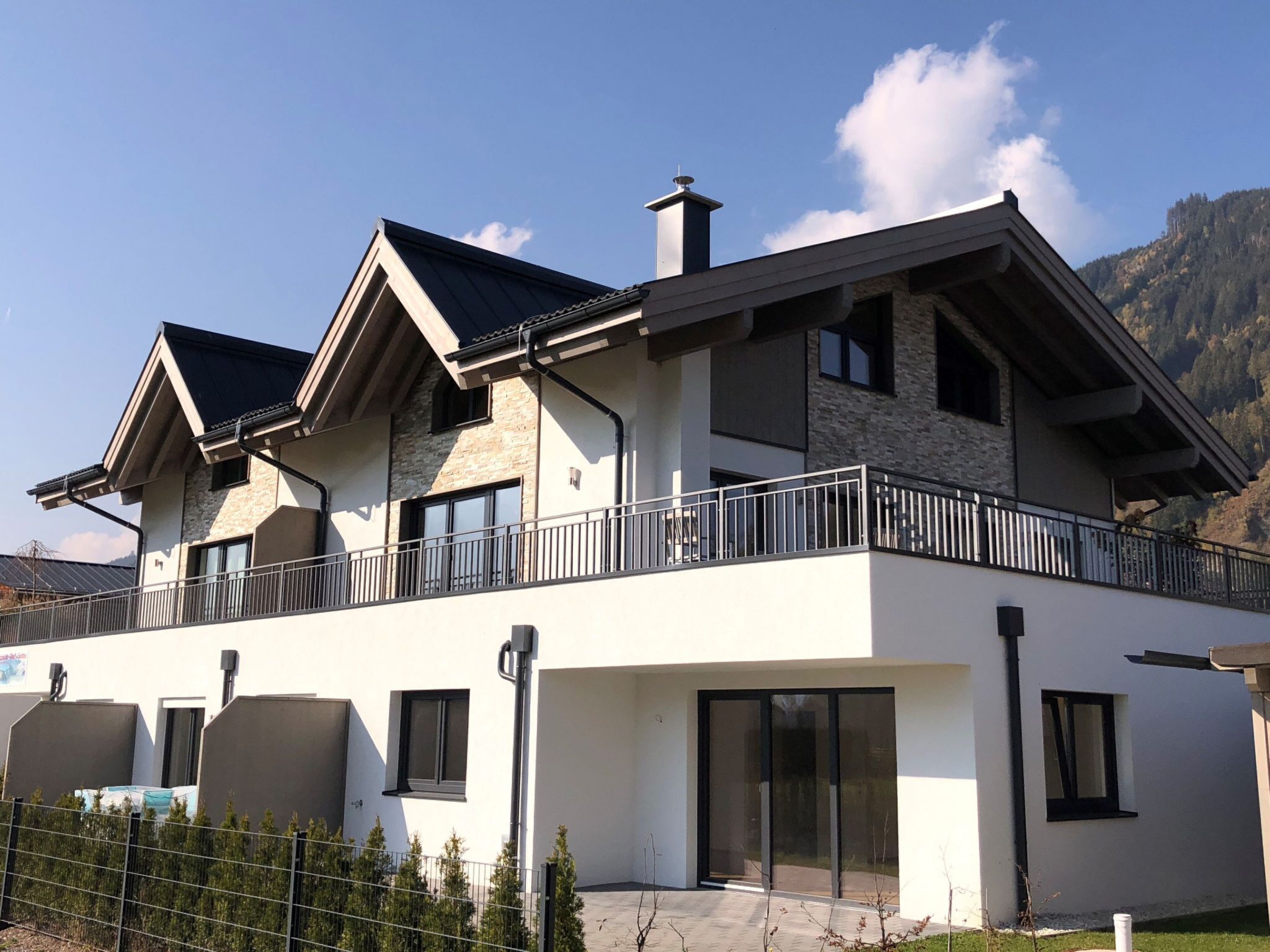 A modern two-story house with a balcony, large windows, and a stone facade.