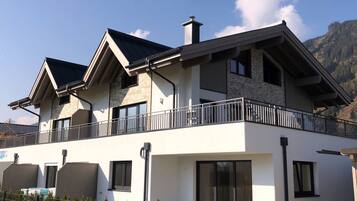 A modern two-story house with a balcony, large windows, and a stone facade.
