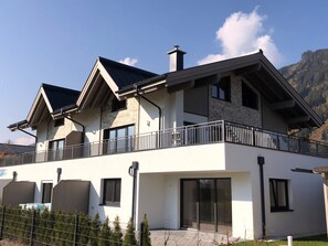 Ein modernes, zweistöckiges Haus mit Balkon, großen Fenstern und einer Steinaußenwand.