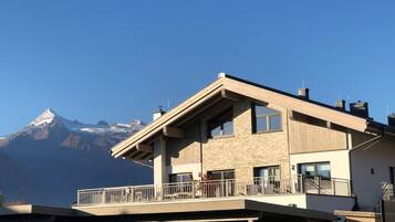 A modern two-story building with a balcony, a mountain view, and a parking area.