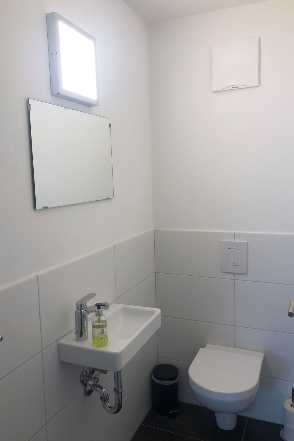 A small, white bathroom with a white sink, a toilet, and a mirror on the wall.