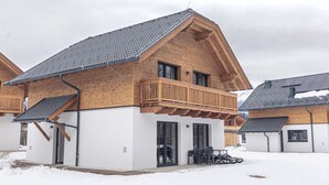 A wooden chalet with a balcony, a covered patio, and a snow-covered ground. - 6_ALP - Chalet Speiereck 5 by Interhome (Mariapfarr)