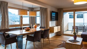 A modern hotel room with a dining area, a flat-screen TV, and a balcony with a view of the mountains. - 3_SPA Panorama MAX 205 by Interhome (Zell am See)