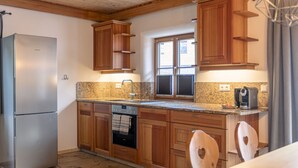Una cocina con gabinetes de madera, un refrigerador de acero inoxidable, un horno empotrado y un piso de baldosas de piedra.
