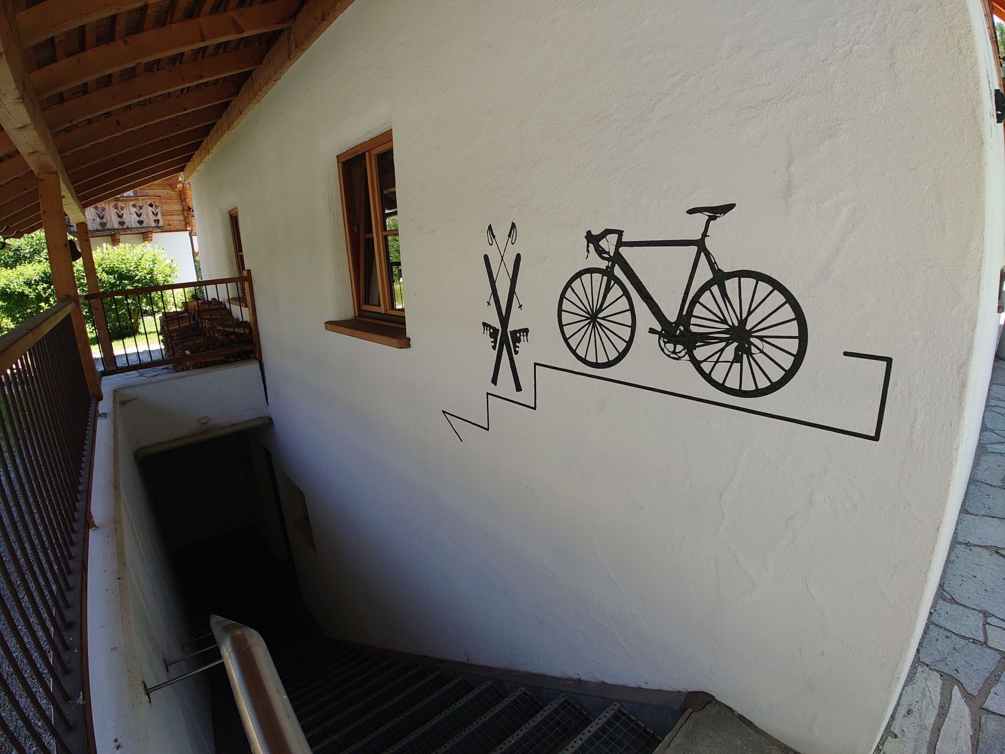 Un escalier menant à un espace abrité, orné d’un symbole de vélo fixé au mur, avec une fenêtre et une porte.