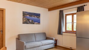 Una cocina moderna con un sofá gris, piso de madera, un ventanal con cortinas y un cuadro colgado en la pared que muestra un lago.
