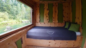 Una habitación de cabaña de madera con una cama, una ventana y vista a un bosque.