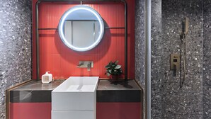 A modern bathroom with a round mirror, a white sink, and a red accent wall. - Life Style  (Douala)