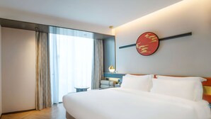 A hotel room with a large bed, a bedside table, a wall-mounted artwork, and a window with curtains. - Life Style  (Douala)