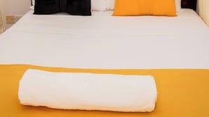 Cama bem arrumada com colcha branca e amarela, dois travesseiros e toalha branca enrolada.