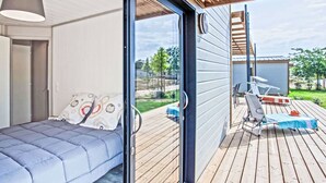 Un dormitorio moderno con cama, puerta corrediza de vidrio que da a una terraza exterior con mesa y sillas.