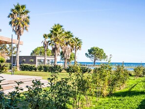 A modern building with a glass facade, surrounded by lush greenery and palm trees, with a clear view of the sea. - Lodge Premium 6p by Interhome (Santa Maria-Poggio)
