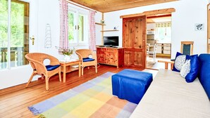 Una habitación con paneles de madera, un sofá, sillas, un televisor y una zona de cocina.