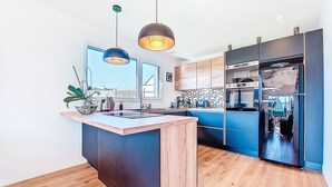 Une cuisine moderne dotée d’un îlot central, de meubles en bois, d’un réfrigérateur encastré et de luminaires suspendus.