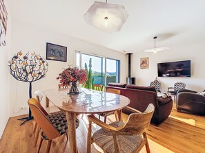 A modern living room with a round dining table, wooden chairs, a sofa, and a television. - Ty Coat by Interhome (Plonéour-Lanvern)
