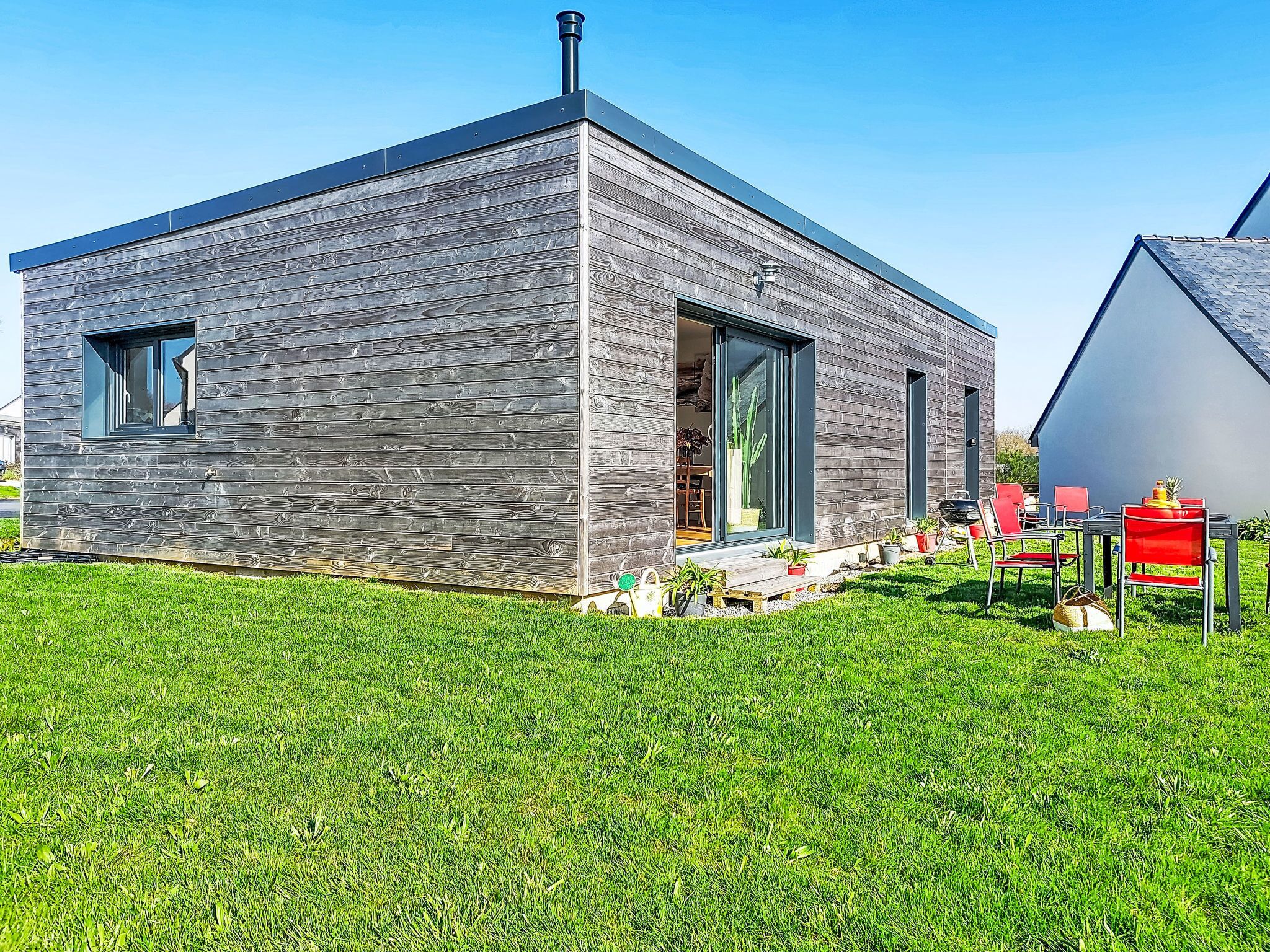 Een modern huis met een schuin dak, schoorsteen en een klein terras met potplanten.