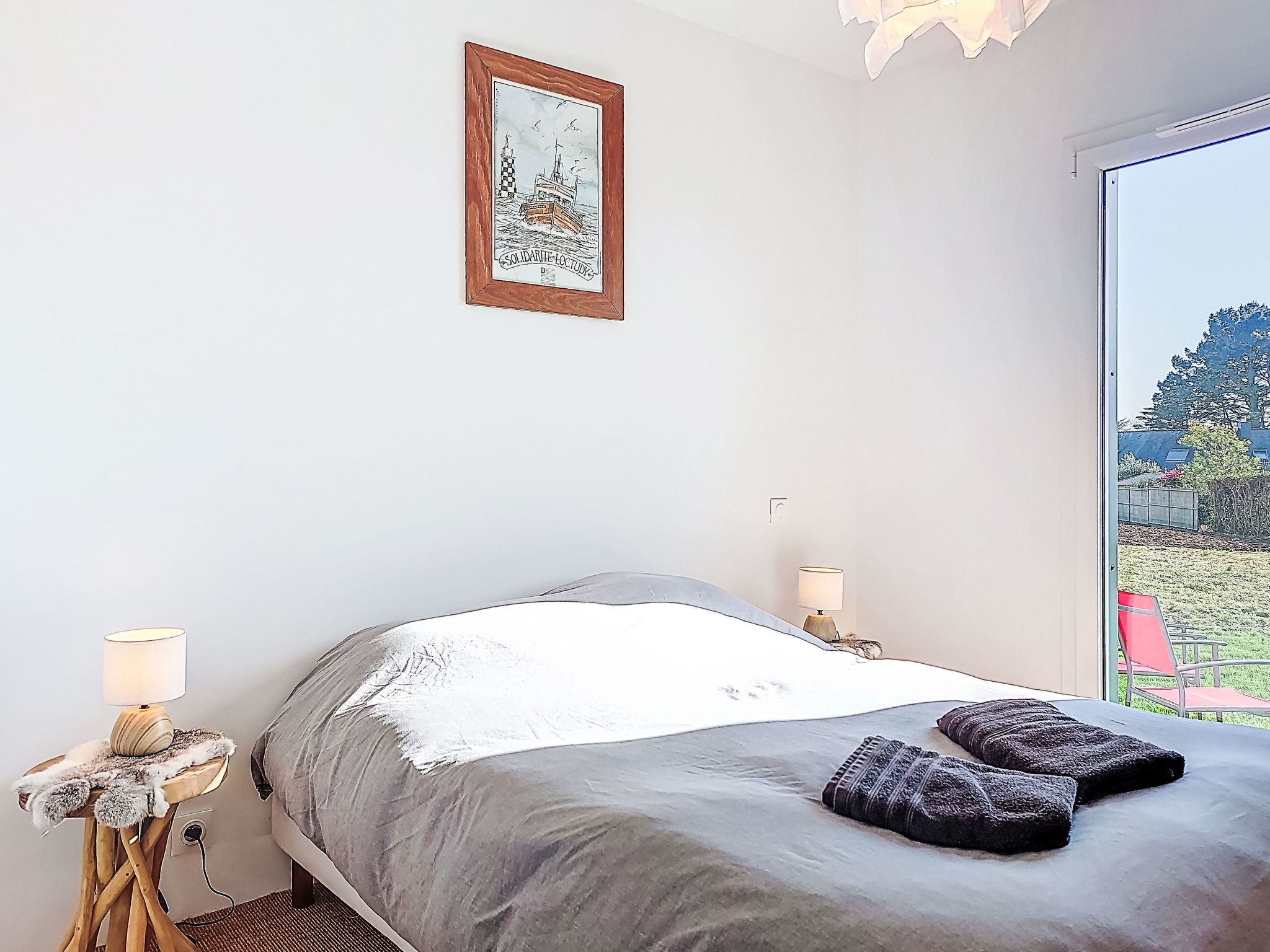 Een slaapkamer met een bed, een bedlampje, een lijst met een afbeelding en uitzicht op een tuin.