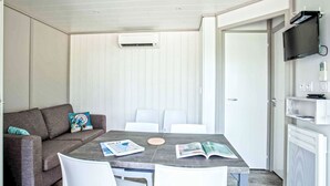 Ein Zimmer mit grauem Sofa, weißen Stühlen, einem Tisch mit Zeitschriften, einem an der Wand montierten Fernseher und einer Tür.