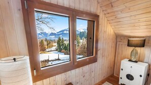 Une pièce de cabane en bois avec une grande fenêtre, un petit meuble blanc et une lampe.