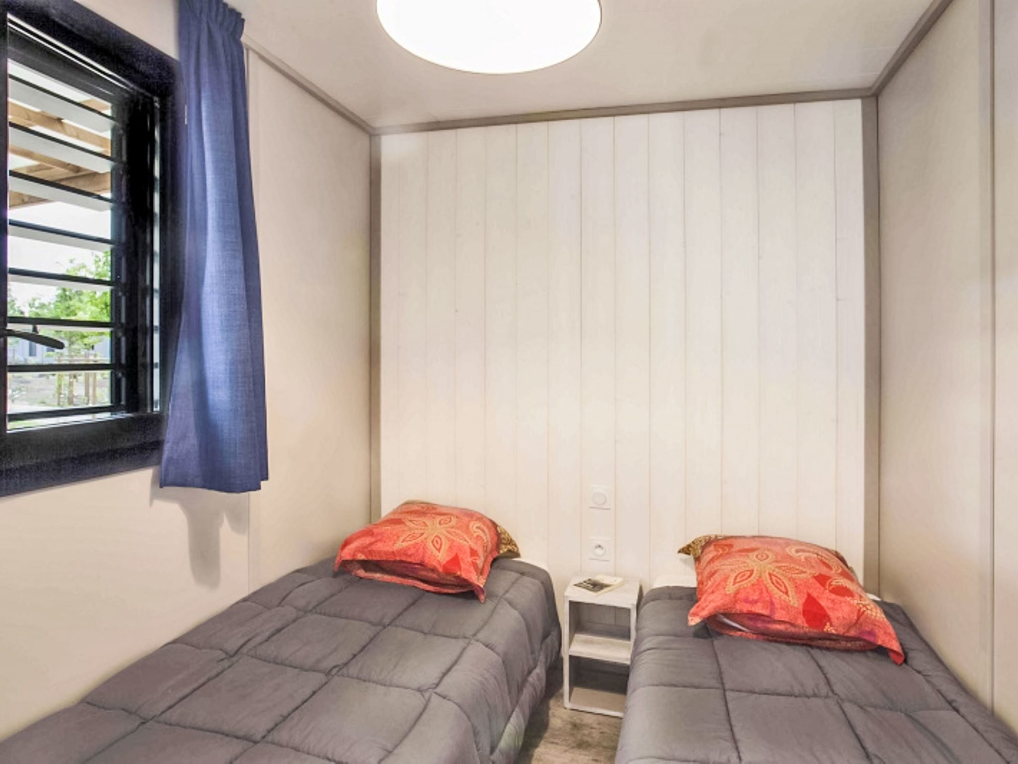 Eine kleine, einfache Unterkunft mit zwei Einzelbetten, einem Fenster mit Jalousien und einer weißen Decke.