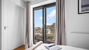 Quarto com uma janela grande, uma cama e vista para uma área residencial.