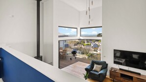 Uma sala de estar moderna com uma televisão grande, um sofá e uma varanda com vista para as casas.
