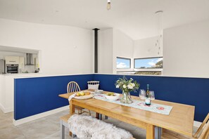 A modern kitchen with white cabinets, a wooden dining table set with plates, a vase with flowers, and wine glasses.