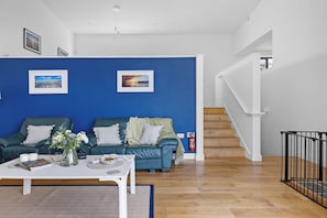 A living room with a blue accent wall, a green sofa, a white coffee table, and a staircase.