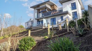 Uma casa moderna de dois andares com varanda, cerca de madeira e jardim.
