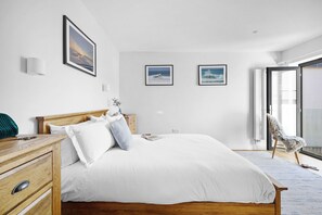 A bedroom with a wooden bed, white bedding, a wooden nightstand, a chair, and two framed pictures on the wall.