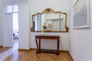 A room with a wooden floor, a large ornate mirror on the wall, a small table with a vase, and a painting. - iFlat | Classic roman palazzo Fons Trevi A15 (Rome)