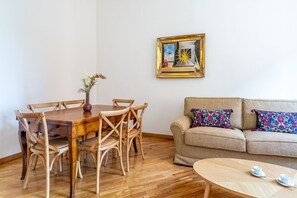 Un comedor con una mesa y sillas de madera, un jarrón con flores, un sofá con cojines estampados y una obra de arte enmarcada en la pared.