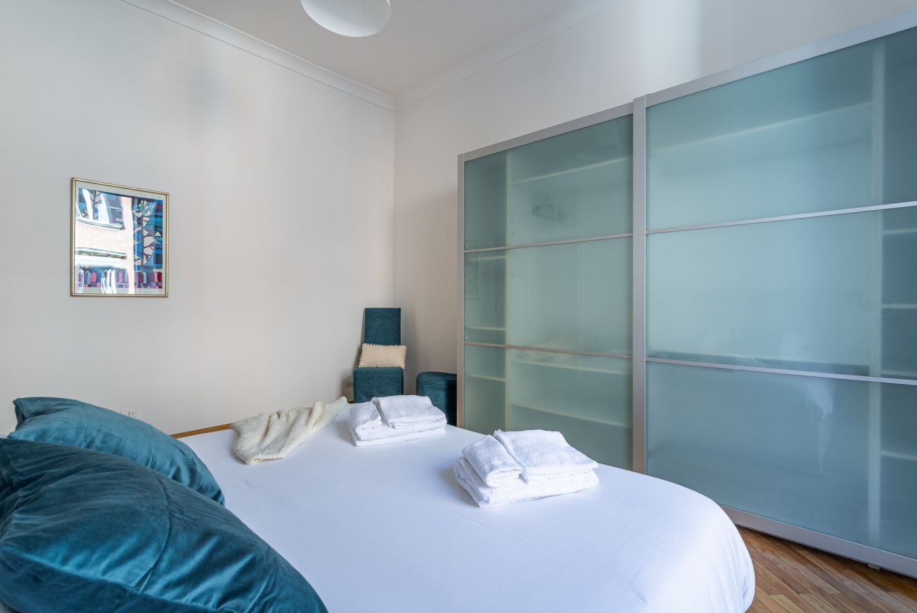 A modern bedroom with a bed, pillows, a bedside table, a chair, and a large sliding glass door.